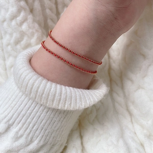 Handmade red braided cord bracelets with 18K gold-plated beads on a model's wrist