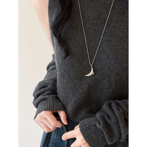 Close-up of textured moon pendant on long silver sweater chain worn on dark knitwear