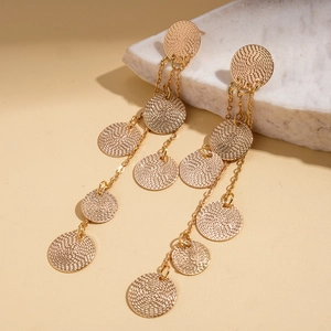 Detailed view of layered gold tassel earrings with textured round metal discs on marble