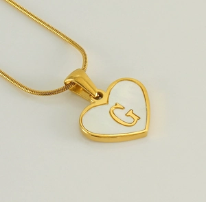 Macro detail of 18K gold heart pendant with white shell inlay and relief letter G