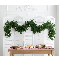 Close-up of green Christmas garland with warm LED lights on a white shutter screen