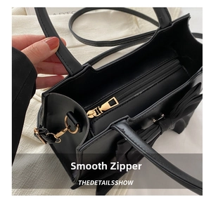 Detail showing smooth gold zipper and bow accent on black leather shoulder bag