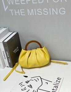 Detail of yellow pleated cloud bag with wooden handle and gold chain shoulder strap