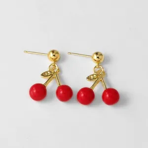Macro detail of gold-plated cherry drop earrings with red beads and engraved leaf