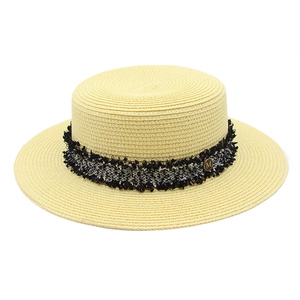 Detailed macro view of woven boater hat featuring fringe ribbon and gold M letter metal logo