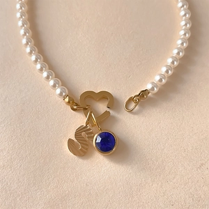 Vue détaillée d'un collier de perles avec pendentif lettre 'S' et cristal bleu brillant