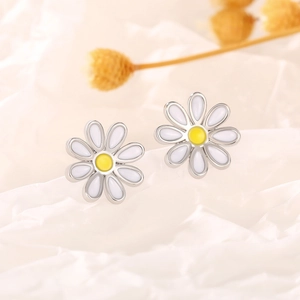Macro close-up of daisy stud earrings with white petals and yellow centers on white fabric