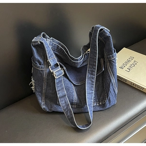 Détail du sac en jean bleu montrant les bords effilochés et la large bandoulière réglable