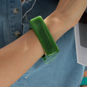 Close-up of a green acrylic square bangle bracelet worn over a blue denim shirt