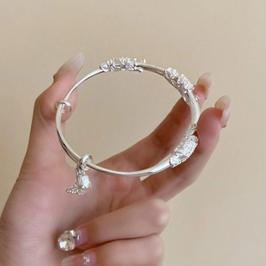 Close-up of silver lotus bamboo bangle with butterfly charm and floral engraving