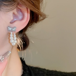 Detail of silver bow earrings with sparkling rhinestones and dangling faux pearls on model