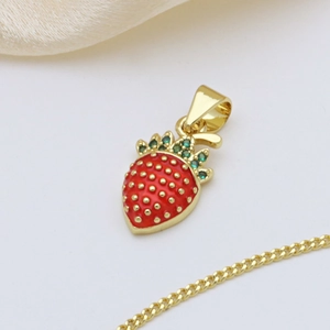 Golden strawberry pendant necklace with red enamel and green crystals on silk background