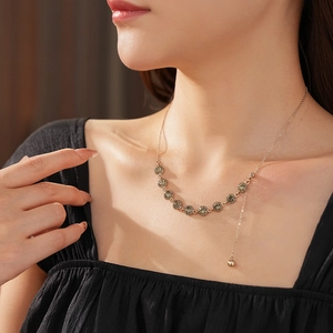 Close-up of a French style gold necklace featuring a deep green round gemstone on a model