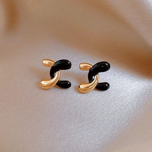 Detailed view of gold and black crisscross stud earrings on premium champagne silk fabric