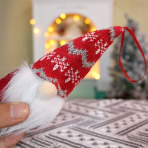 Detail of Christmas gnome pendant with red knitted hat held in hand by a decorated tree