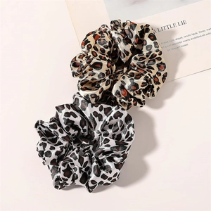 Detail view of brown and white leopard print satin hair scrunchies on a neutral table