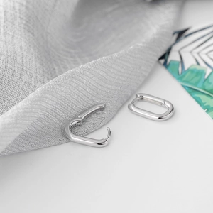 Élégantes boucles d'oreilles ovales en argent S925 poli sur fond de tissu gris texturé