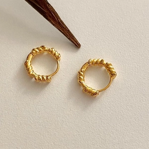 Detailed view of golden twisted hoop earrings on a textured minimalist background