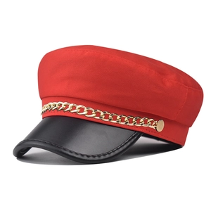 Detail of red newsboy hat featuring black leather visor and gold metal chain trim