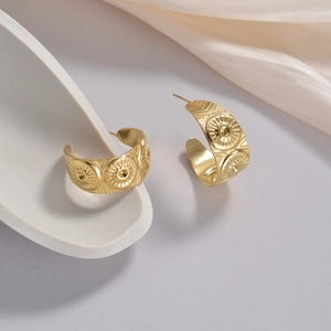 Macro view of gold C-shape earrings with sunburst relief pattern and retro texture