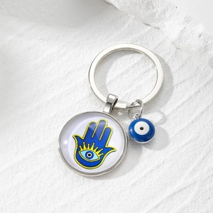 Hamsa Hand and Evil Eye glass keychain with silver pendant on stone texture background