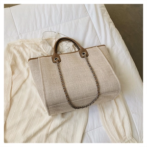 Detailed view of beige textured tote bag with brown leather handles and gold chain strap