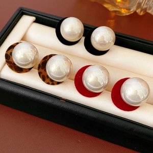 Detailed view of pearl earrings with leopard, black, and red velvet backings in a box