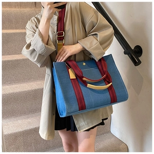 Detail of blue denim tote bag with red strap and leather handles worn on shoulder