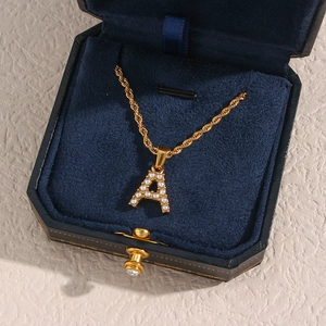 Macro shot of 18K gold plated twist chain and pearl letter A pendant in a jewelry box