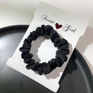 Minimalist black velvet scrunchie displayed on white card over elegant dark backdrop
