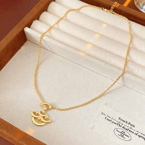 Détail du collier avec pendentif feuille en éventail doré dans son écrin de luxe en velours