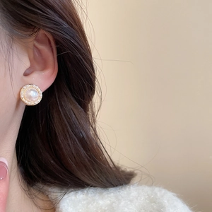 Close-up of elegant pearl stud earring with gold rim and micro-inlay worn by a model