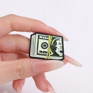 Broche en émail dessin animé de billets de banque tenue à la main en gros plan