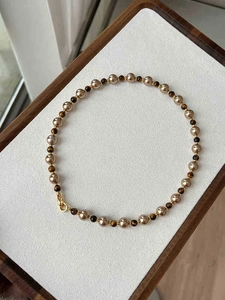 Détail d'un collier de perles dorées et pierres œil de tigre sur plateau en velours