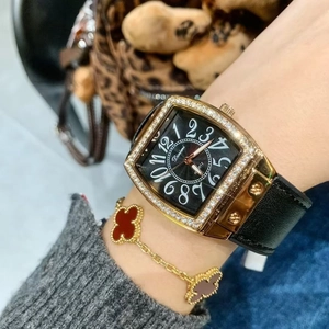 Close-up of a women's square gold watch with black leather strap and clover bracelet
