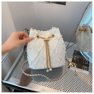Detail of white denim bucket bag with quilted fringe, gold chain, and pearl drawstrings