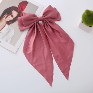 Close-up of rose pink satin bow hair clip with long ribbons on white background