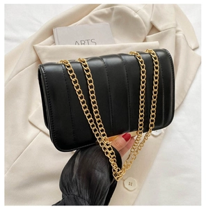 Close-up of black quilted crossbody bag with elegant gold chain strap held by model