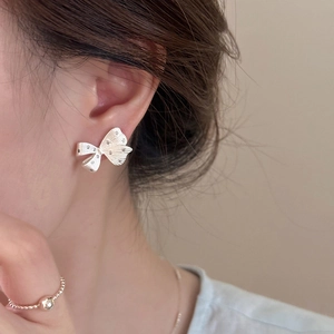 Close-up of a silver bow earring with textured details worn by a model for a chic look