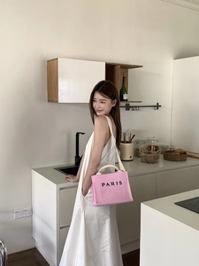 Close-up of pink woven tote bag with Paris lettering shown on a model in a kitchen