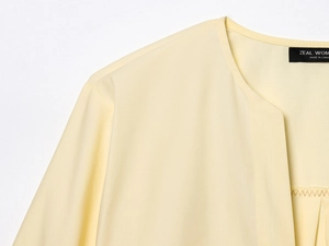 Close-up of pale yellow poplin shirt collar with ZEAL WOMAN brand label detail