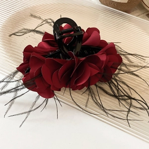 Close-up of deep red pleated petals and black feather accents on a glossy hair claw clip