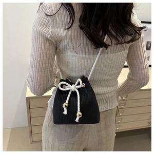 Close-up of black knitted bucket bag with large white bow and gold bead drawstring