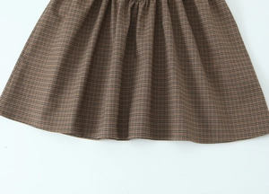 Close-up of brown plaid pleated dress hem showing fine textile texture and stitching