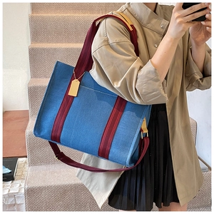 Detail of blue denim tote bag with brown straps and gold hardware worn on shoulder