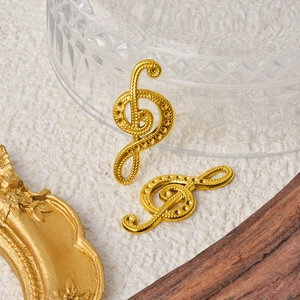 Macro view of two golden treble clef musical note pendants on beige textured fabric