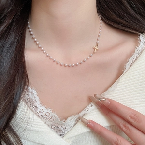 Detailed view of a French pearl necklace with a minimalist gold cross pendant on a model