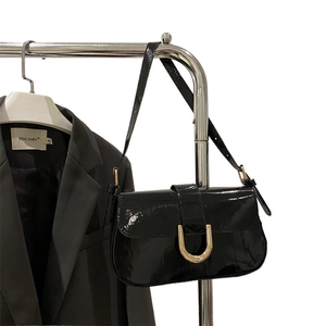 Glossy black patent leather handbag with gold horse buckle on a stylish shoulder bag