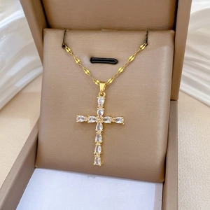 Macro shot of gold cross necklace with pear-cut zircon stones on beige jewelry box