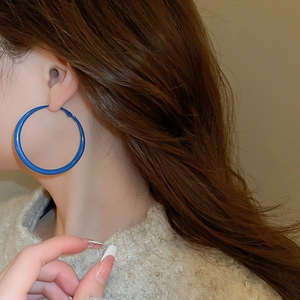 Detail of a large Klein blue round hoop earring worn by a model to show size and style